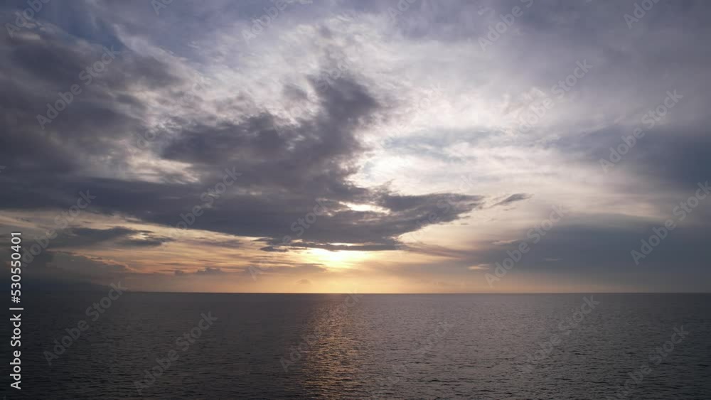 Low sun shine from behind dark clouds, calm sea water seen down. Peaceful and quiet view of sea at sunset hour. Neat colors of on the sky, small ripples move at water surface Low sun shine from behind dark clouds, calm sea water seen down. Peaceful and quiet view of sea at sunset hour. Neat colors of on the sky, small ripples move at water surface