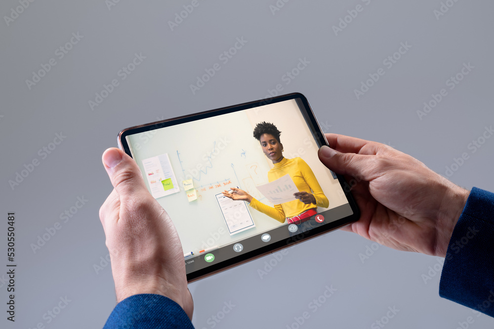 Hands of caucasian businessman making video call on tablet with diverse female colleague on screen