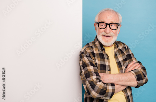 Photo of funky pretty man pensioner dressed checkered shirt eyewear arms folded billboard empty space isolated blue color background