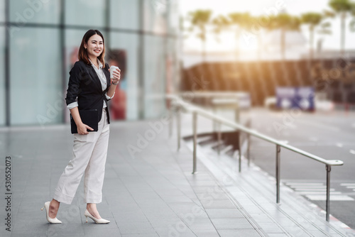 Free Download Young Asian businesswoman using tablet in airport before business trip. Beautiful woman passenger has mobile call and discusses something with smile, holds coffee in hand - GFXLoad
