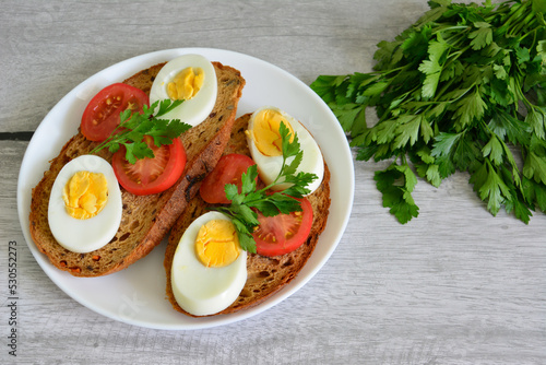 healthy toasts with boiled eggs and tomatoes on white plate, close-up
