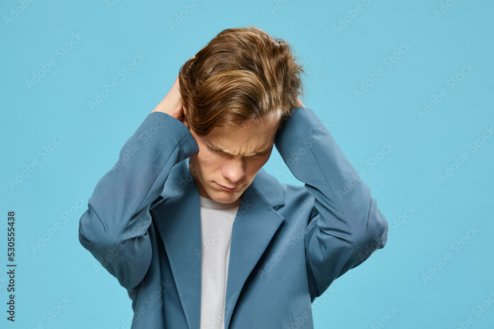 a young man in a classic suit covers his ears with his hands and frowns his face, lowering it down a young man in a classic suit covers his ears with his hands and frowns his face, lowering it down