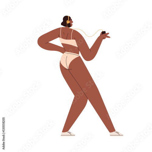 Happy girl listening to music in headphones. Young black woman in bikini danc...