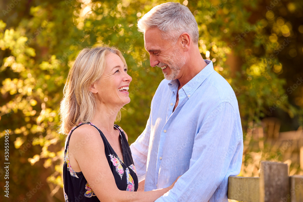 Loving Mature Couple Leaning On Fence On Walk In Countryside Together