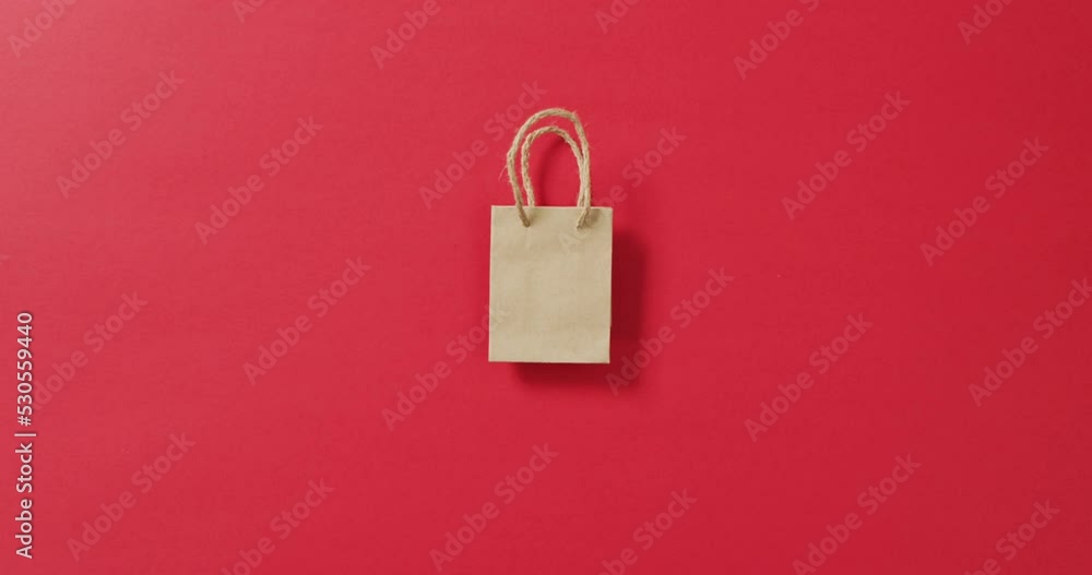 Small brown gift bag with string handles on red background with copy space