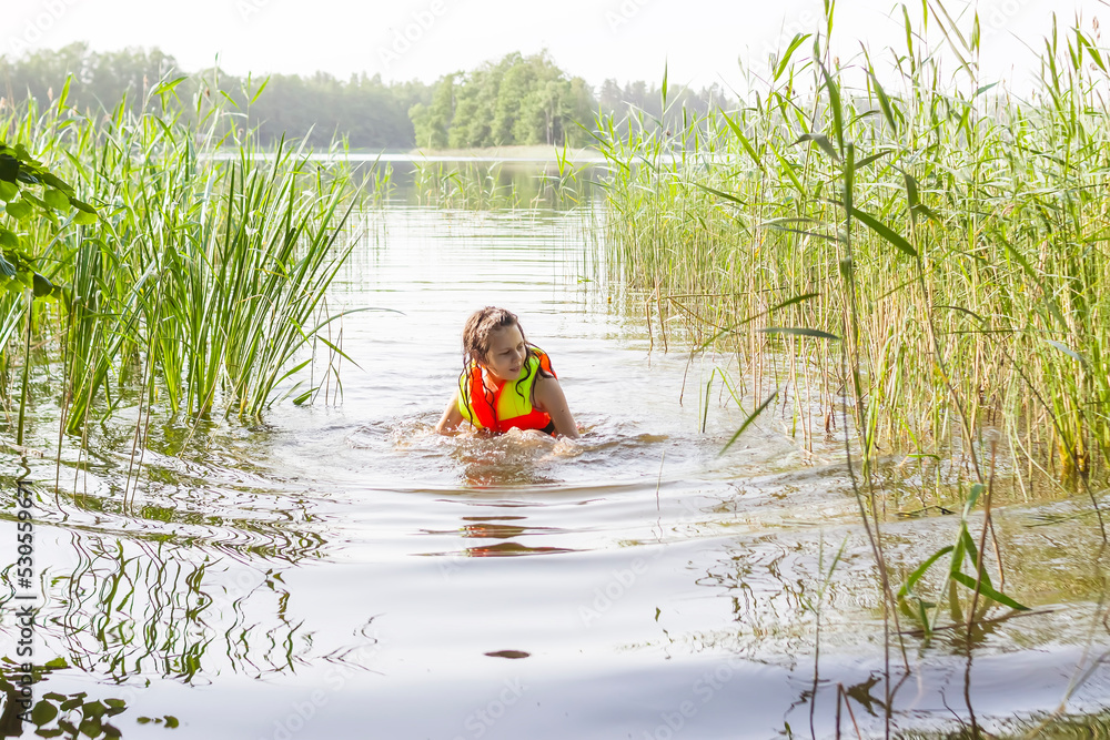 School-age girl wearing life jacket during wild swimming in a lake. School-age girl wearing life jacket during wild swimming in a lake.
