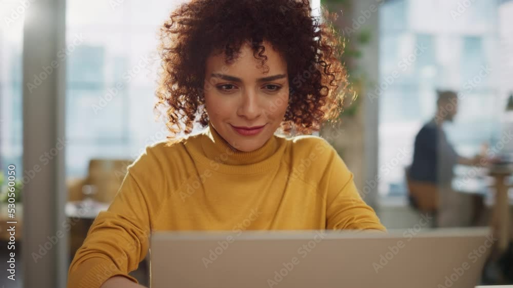 Close Up Portrait of a Happy Middle Eastern Manager Sitting at a Desk in Creative Office. Young Stylish Female with Curly Hair Using Laptop Computer in Marketing Agency.