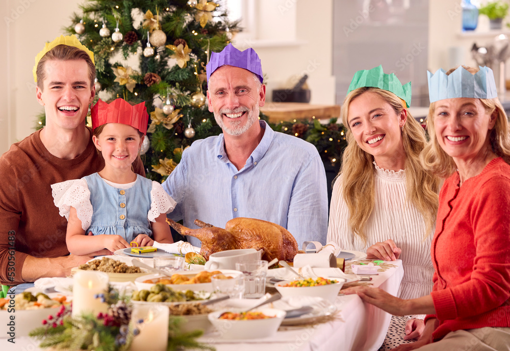 Portrait Of Multi-Generation Family Celebrating Christmas At Home Wearing Paper Hats Before Meal