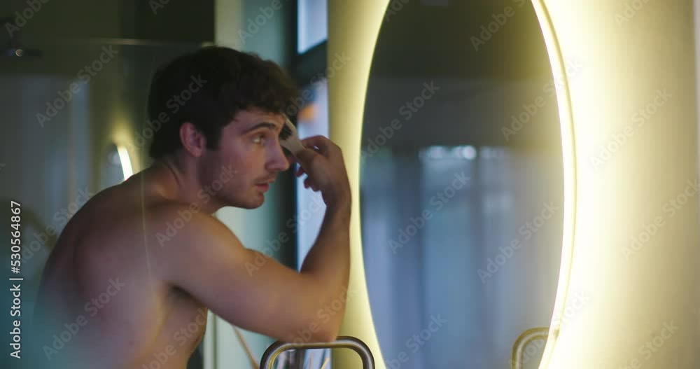 Young man brushes fluffy hair looking at mirror reflection Young man brushes fluffy hair looking at mirror reflection
