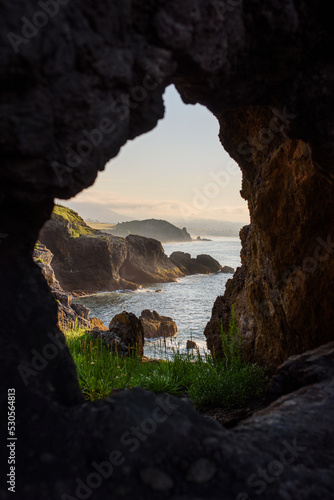 Impressive landscape of cliffs and sea at sunset through a hole in the rock. Caravia, Asturias, Spain photo