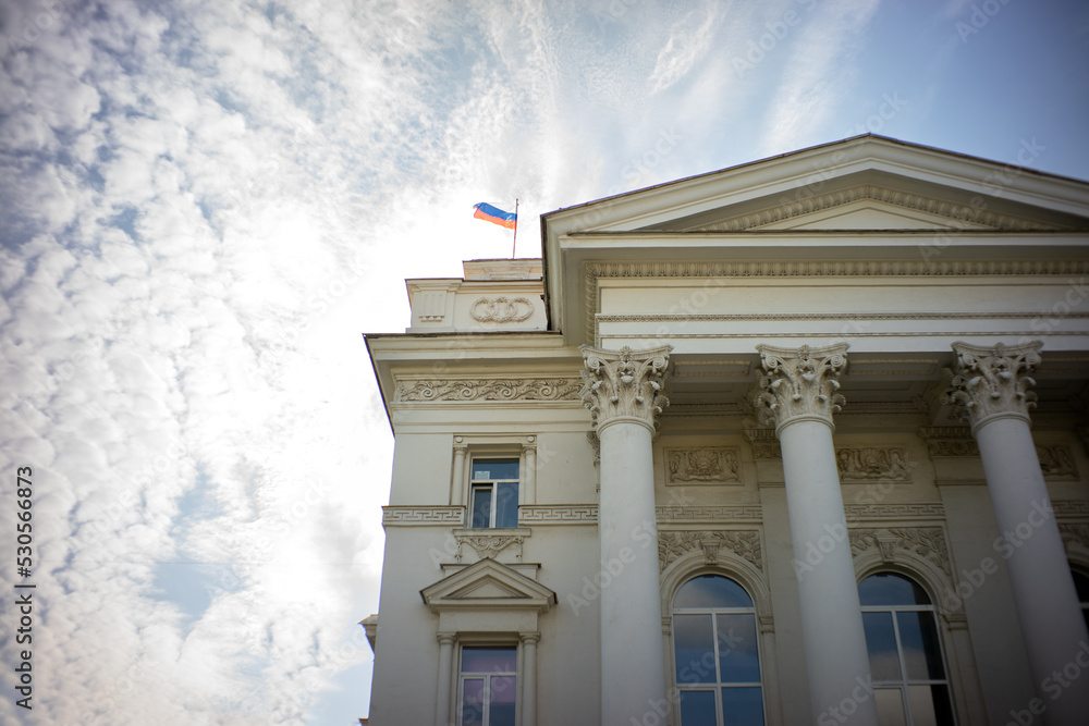 Front view of an administrative building with classical Greek columns, The tricolor flag of Russia is waving against the sky.