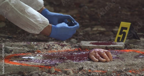 A detective wearing a protective suit and gloves takes pictures of the gruesome scene with the severed hand photo