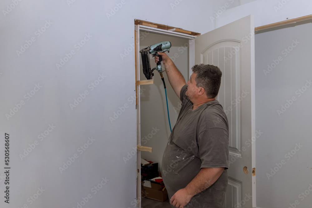 In a new house, an interior door is installed by a trim carpenter using pneumatic nailers