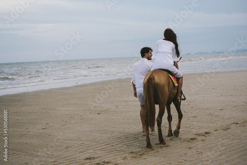 Young asian couple walking with horse on the beach in sunny summer day.