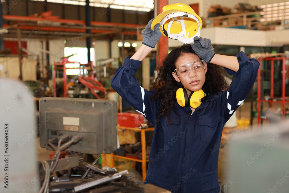 Technician engineer or worker woman in protective uniform maintenance operation or checking lathe metal machine while wipe the sweat away at heavy industry manufacturing factory. Metalworking concept