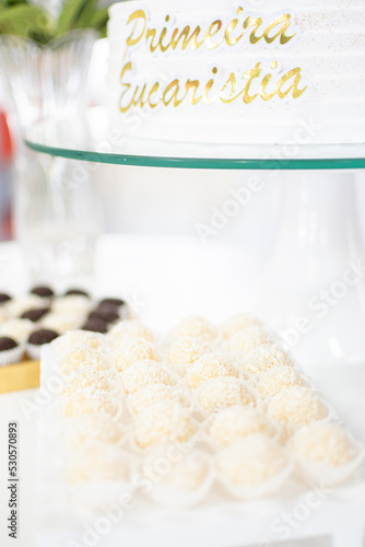 Docinhos alegrando e adoçando as festas. Docinho de festa de coco. Bolo de decorado de primeira eucaristia com escritas douradas. photo