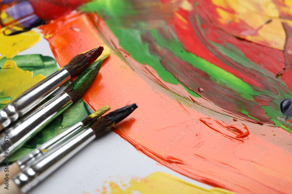 Fototapeta premium Set of brushes with different paints on artwork, closeup. Space for text