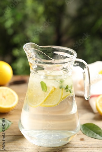 Glass jug of cold lemonade on wooden table