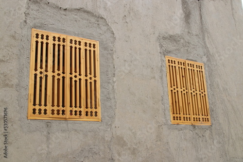 Two wooden yellow windows in grey clay wall arabic style pattern carving photo