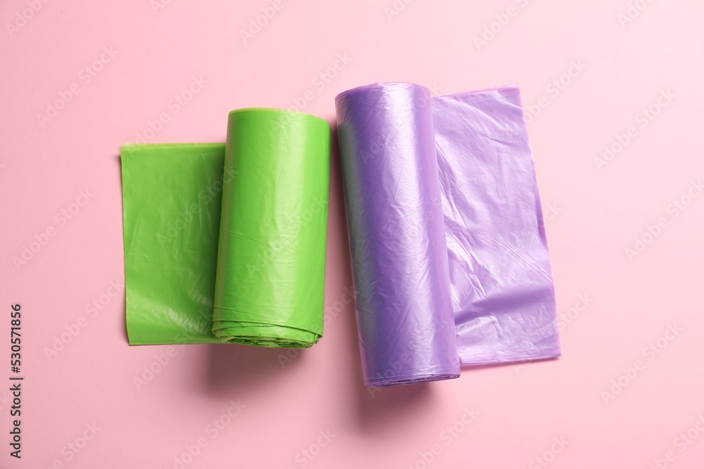 Rolls of different garbage bags on pink background, flat lay