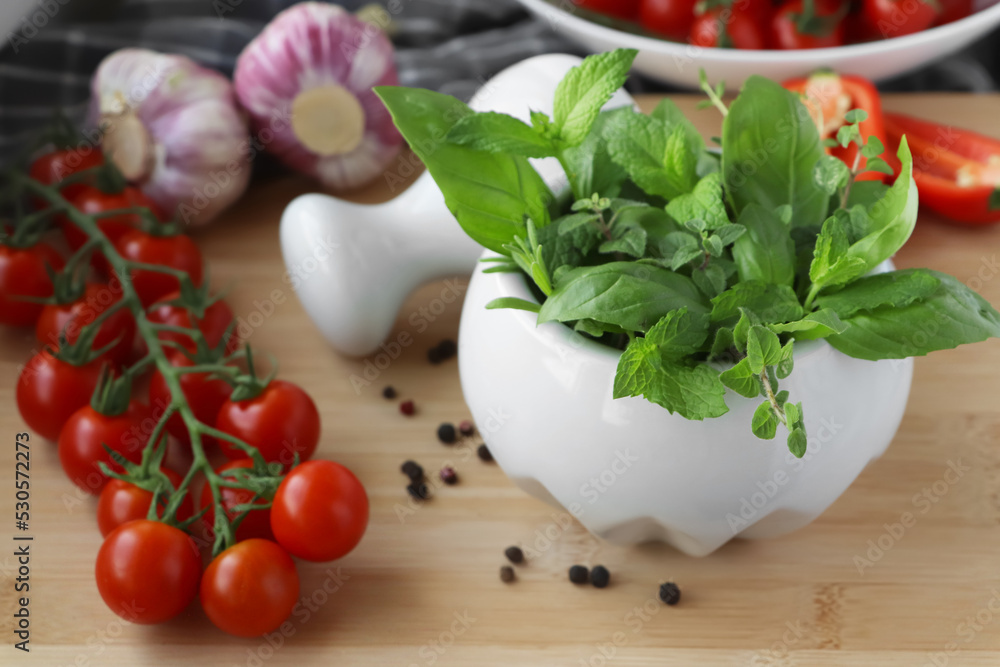 Mortar with different fresh herbs near pepper, garlic and cherry tomatoes on wooden table, closeup Mortar with different fresh herbs near pepper, garlic and cherry tomatoes on wooden table, closeup