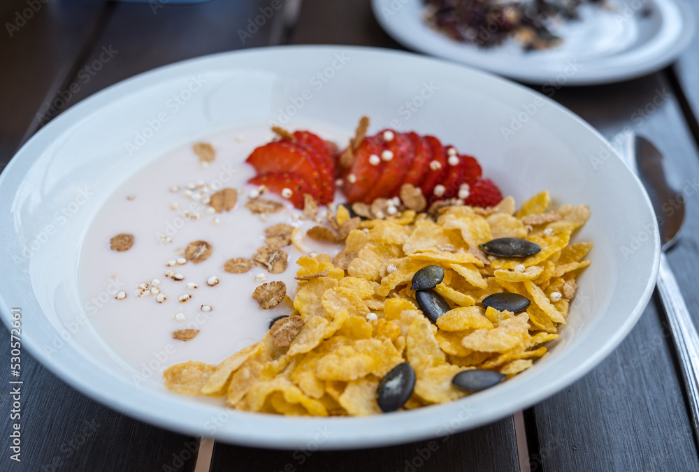 Yogurt bowl with fresh sliced strawberries and dry corn flakes. Breakfast cereal toppings served with spoon on the wooden table. Traditional corn flakes breakfast concept. Healthy eating concept Yogurt bowl with fresh sliced strawberries and dry corn flakes. Breakfast cereal toppings served with spoon on the wooden table. Traditional corn flakes breakfast concept. Healthy eating concept