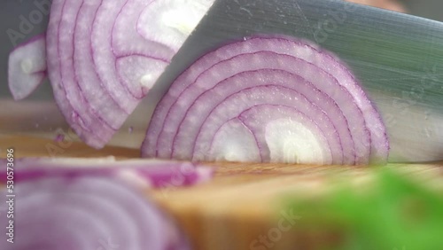 Macro shot hands cut fresh red onion on wooden cutting board on background of vegetables in kitchen. Chop. Cooking food.