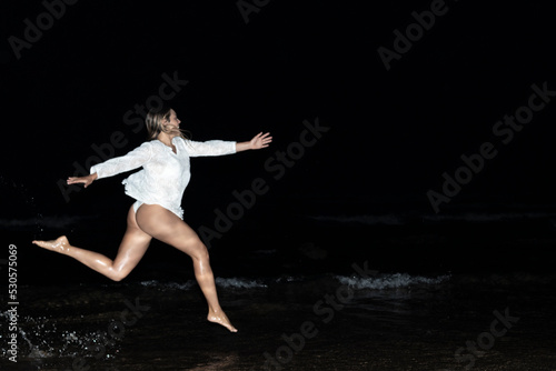 Happy girl running alone on the beach at night in white bikini