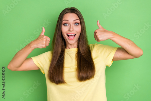 Portrait of satisfied girl with straight hairstyle dressed yellow t-shirt impressed showing thumbs up isolated on green color background