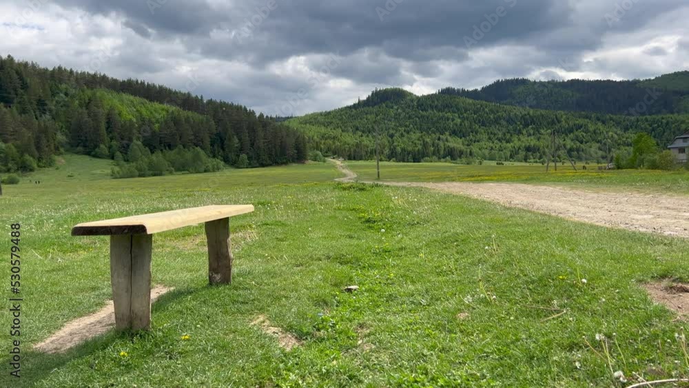 Wooden bench in a green meadow invitation to rest in idyllic place. Amazing cloudy sky, mountain valley, green landscape. Wooden bench on a green meadow with a mountain in background. Wooden bench in a green meadow invitation to rest in idyllic place. Amazing cloudy sky, mountain valley, green landscape. Wooden bench on a green meadow with a mountain in background.