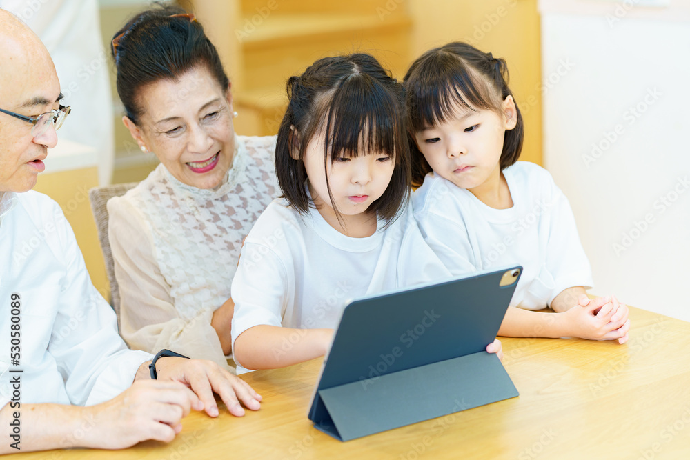 タブレットPCを操作するシニア夫婦と孫たち タブレットPCを操作するシニア夫婦と孫たち