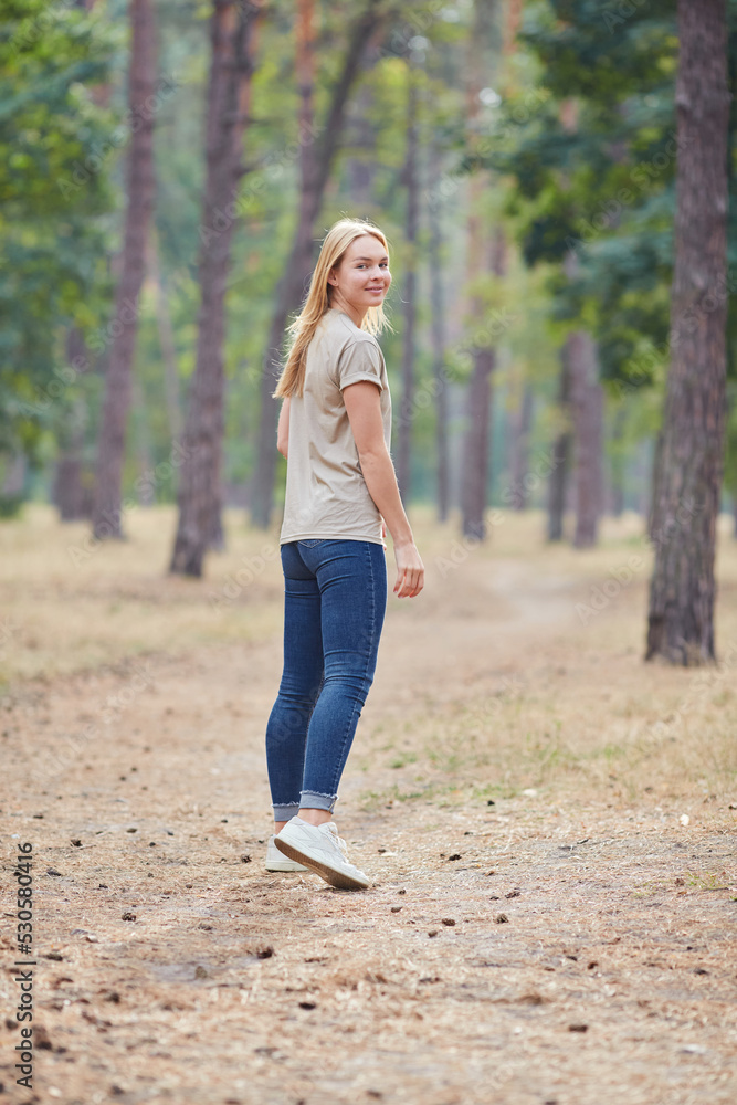 Blue-eyed blonde in a beige T-shirt walks in a pine forest. Portrait of a joyful young woman enjoying in autumn park. Blue-eyed blonde in a beige T-shirt walks in a pine forest. Portrait of a joyful young woman enjoying in autumn park.