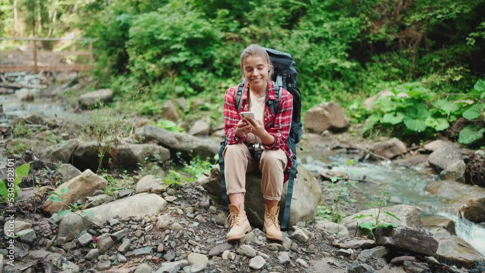 Happy blonde woman tourist typing on mobile near river in the mountains outdoors Happy blonde woman tourist typing on mobile near river in the mountains outdoors