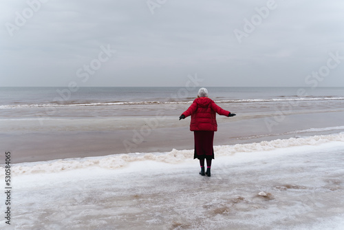 A woman stands looking at the sea spreading her arms to the sides, the view from behind