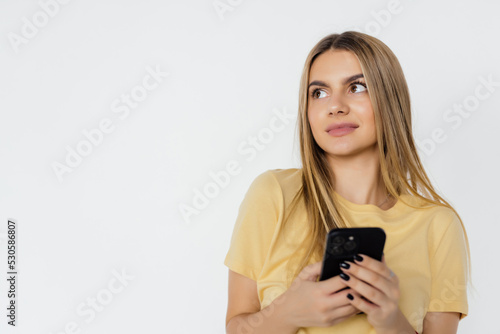 Photo of a young woman posing isolated over white wall background using mobile phone.