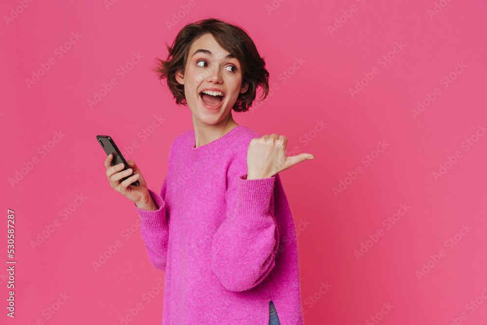 Young excited woman pointing finger aside while using cellphone Young excited woman pointing finger aside while using cellphone