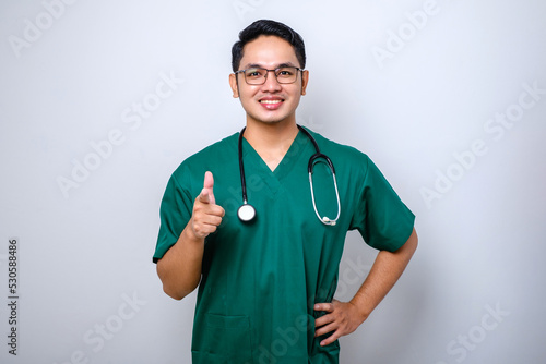 Cheerful handsome, asian male nurse or doctor in green scrubs, stethoscope, pointing camera