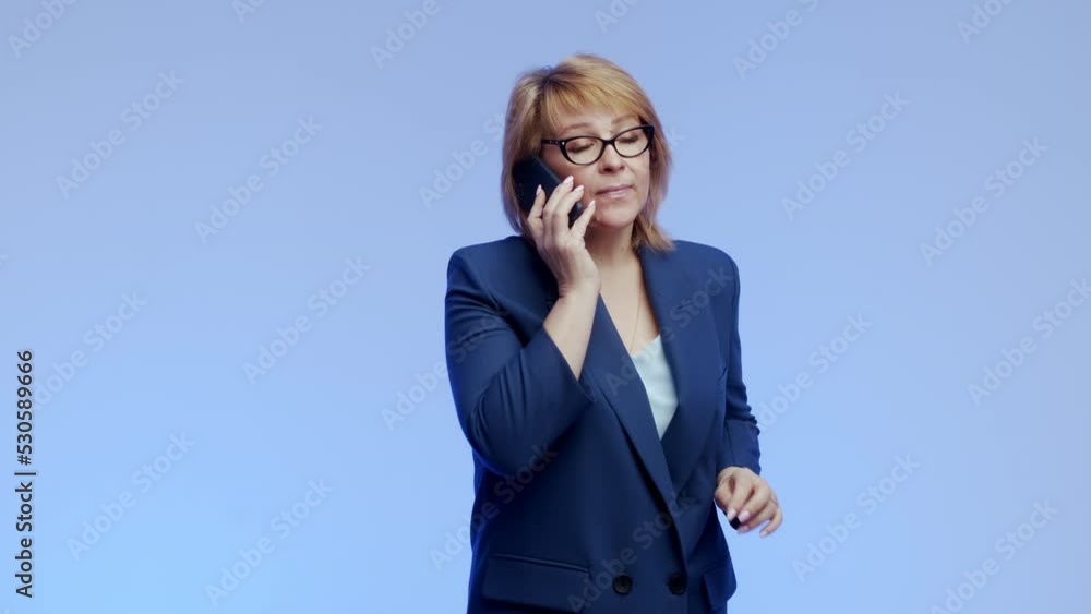 An elderly business woman, an experienced female specialist, is talking on a mobile phone, looking into the frame with a smile, negotiating with a client. Close up portrait of happy mature woman An elderly business woman, an experienced female specialist, is talking on a mobile phone, looking into the frame with a smile, negotiating with a client. Close up portrait of happy mature woman