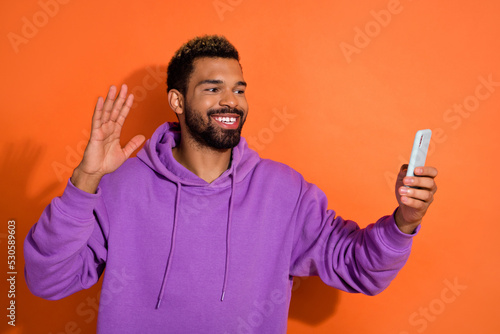 Photo of cheerful person guy influencer make selfie video arm palm wave hi isolated on orange color background