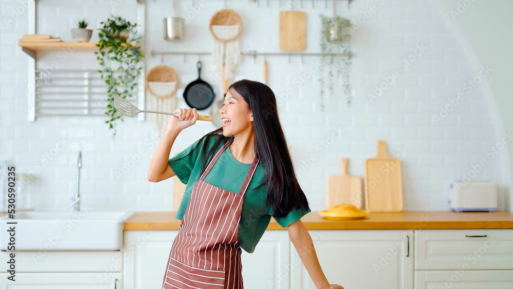 Asian young woman dancing in kitchen room. Female happy and relaxing at free time on weekend Asian young woman dancing in kitchen room. Female happy and relaxing at free time on weekend