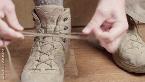 The man puts on brown shoes. A soldier or tourist laces up his boot, close-up