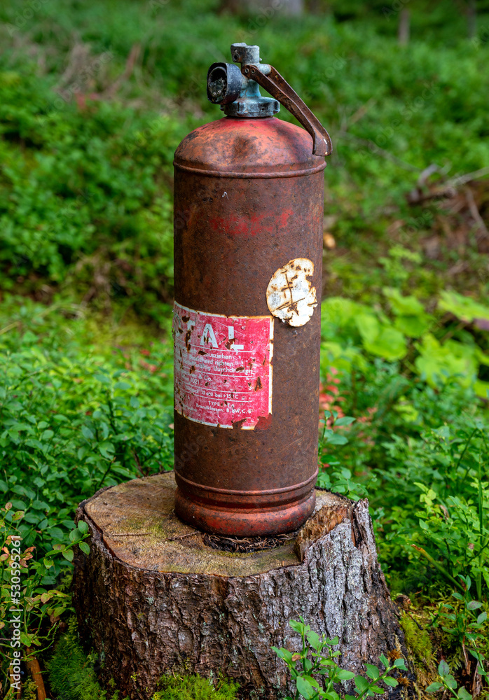 old and rusty fire extinguisher on a tree stump in a forest, Austria old and rusty fire extinguisher on a tree stump in a forest, Austria