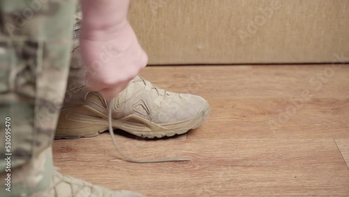 A soldier laces up a sand-colored boot