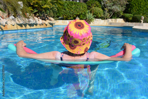 Woman with sunscreen lotion on her shoulders floating on swim noodles in swimming pool