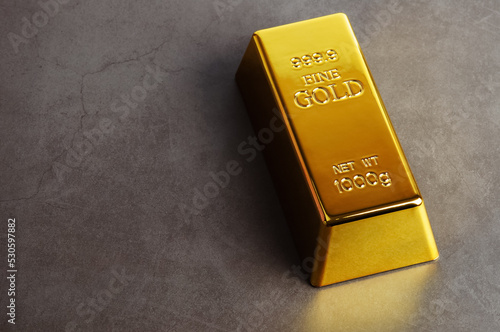 An ingot of gold metal bullion of pure brilliant diagonally located on a gray textured background.