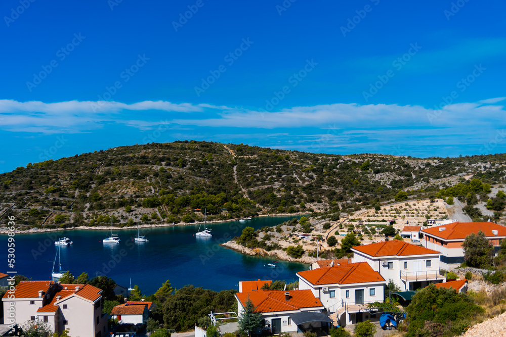 view of a coastline with a small village and sailboats in a bay in Sevid, Croatia