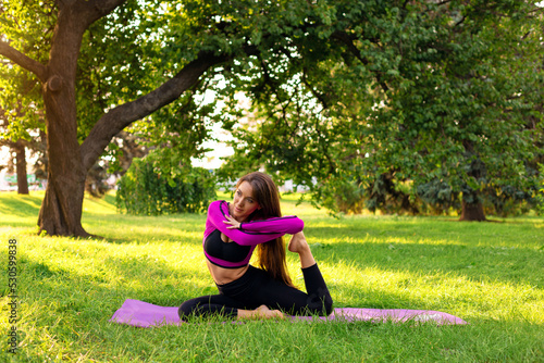 a young woman is doing stretching on a mat in the park. morning meditation in the park © Kateryna
