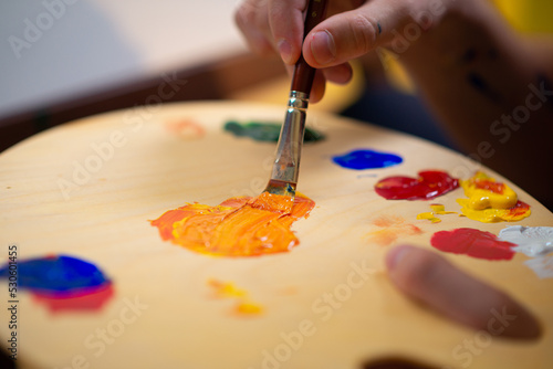 A man is using a flat brush to mix two colours on a palette and paint onto a canvas