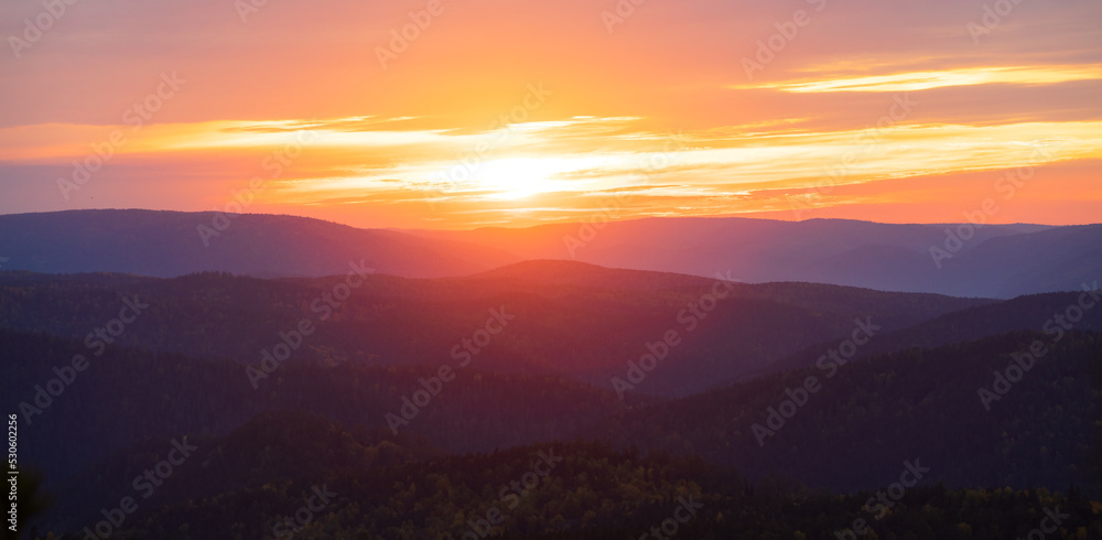 Bright red-orange dawn over a misty mountain forest. Evening landscape on the sunset sky over the Siberian taiga. Colorful sky at foggy morning at sunrise above coniferous forest in mountain