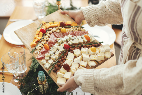 Cheese appetizers and salami in shape of christmas tree, creative food arrangement for christmas holidays. Woman holding cheese board on background of festive table with fir branches. Antipasto